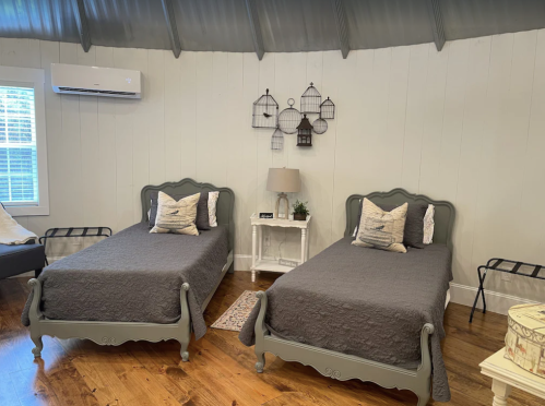 A cozy room with two gray beds, a nightstand, and decorative lanterns on the wall. Natural light from a window.