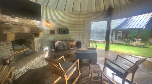 Cozy outdoor seating area with a fireplace, surrounded by a circular metal structure and a view of a green lawn.