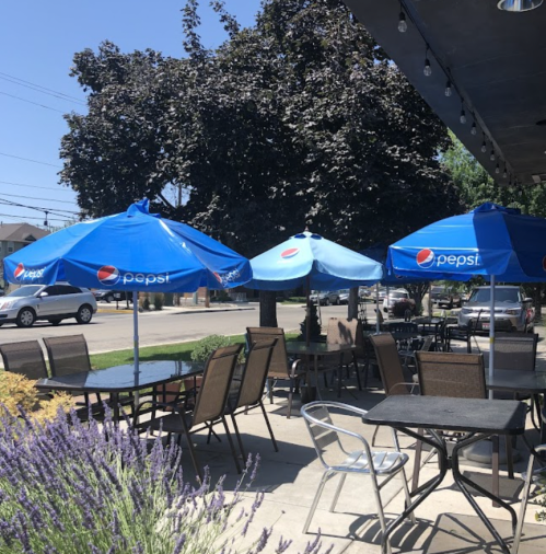 Outdoor seating area with blue Pepsi umbrellas, tables, and chairs, surrounded by greenery and a sunny atmosphere.