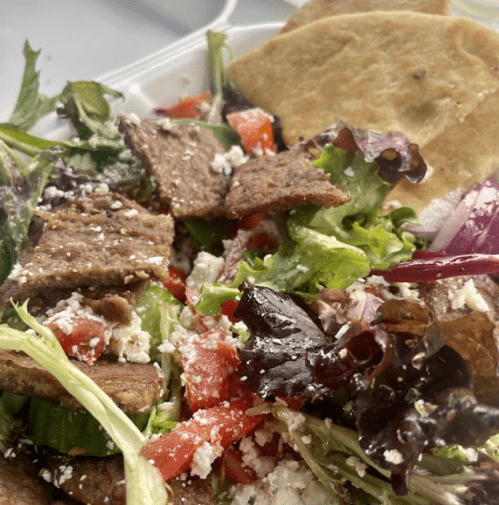 A fresh salad with mixed greens, tomatoes, feta cheese, and slices of grilled meat, served with flatbread.