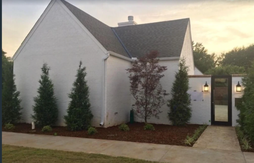 A modern white house with a landscaped front yard, featuring trees and a pathway leading to the entrance.