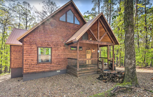 A rustic wooden cabin surrounded by trees, featuring a porch and a sloped roof in a serene forest setting.