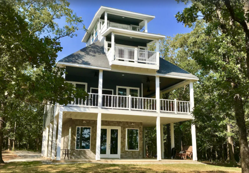 A modern three-story house surrounded by trees, featuring balconies and large windows.