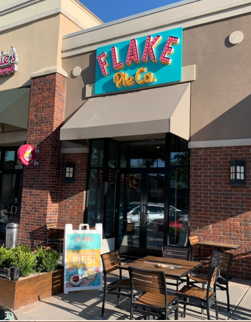 Exterior of Flake Pie Co. with a colorful sign, outdoor seating, and a promotional sign for pies.