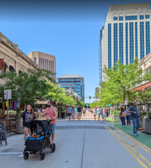 A bustling street market with people walking, stalls on either side, and tall buildings in the background.