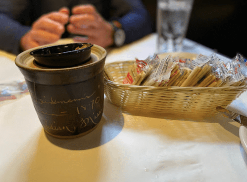 A clay pot with a small lid sits on a table next to a basket of condiment packets.