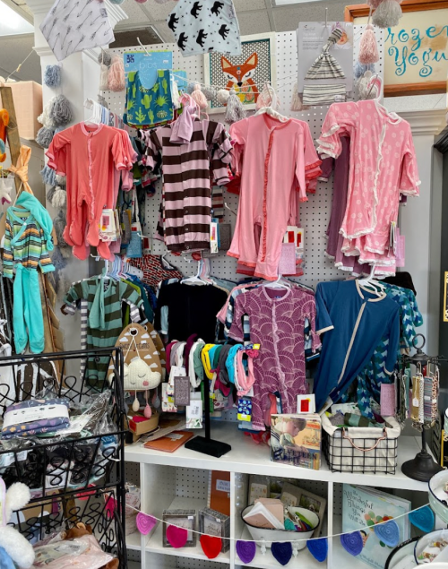 A display of colorful children's clothing, including onesies and accessories, arranged on racks and shelves.