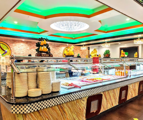 A vibrant buffet restaurant with a colorful ceiling, featuring a variety of food stations and decorative elements.