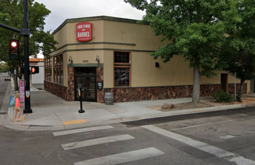 A corner building with a sign reading "Luck Stock and Barrel," featuring stone accents and nearby traffic signals.