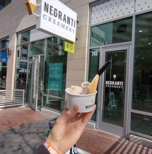 A hand holds a cup of ice cream with a cone outside Negranti Creamery, featuring a modern storefront.