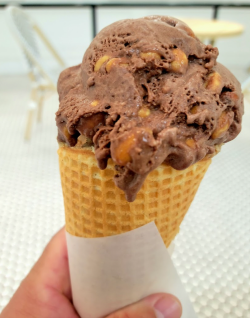 A hand holding a waffle cone filled with chocolate ice cream and nuts.