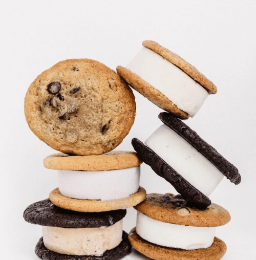 A stack of ice cream sandwiches made with chocolate chip and Oreo cookies, arranged playfully against a white background.