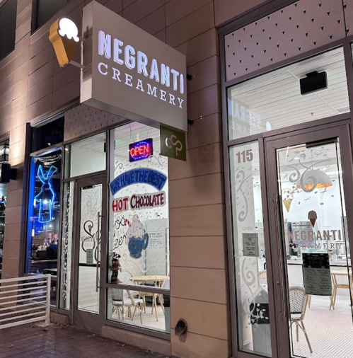 Exterior of Negranti Creamery with illuminated sign, open door, and seating visible through large windows at night.