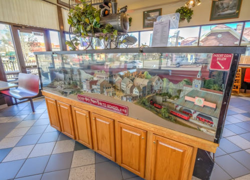 A display case featuring a miniature village scene with buildings and a train, located in a restaurant.