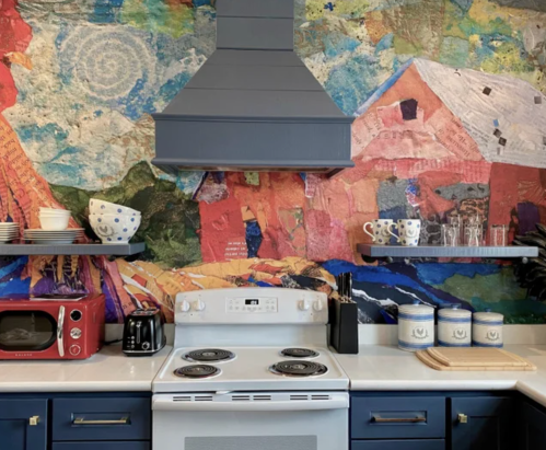 A colorful kitchen featuring a vibrant mural, white stove, red microwave, and blue cabinets with open shelves.