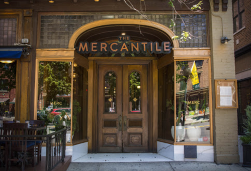 Entrance of "The Mercantile" with wooden doors and large windows, showcasing a welcoming atmosphere.
