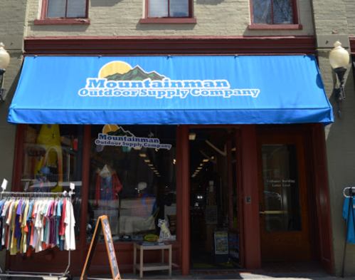 A storefront with a blue awning reading "Mountainman Outdoor Supply Company" and outdoor gear displayed outside.