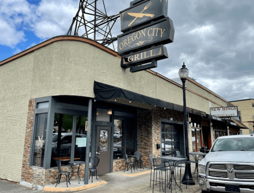 Exterior of Oregon City Grilla restaurant with outdoor seating and a sign, under a cloudy sky.