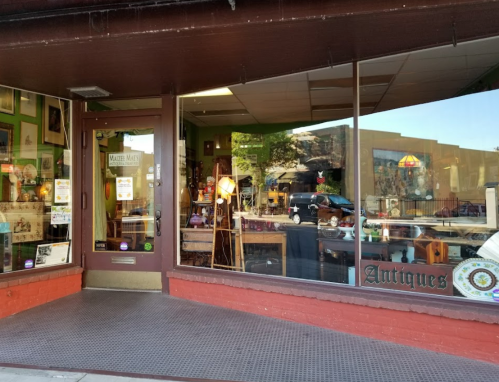 A storefront of an antique shop with large windows displaying various vintage items and decor.