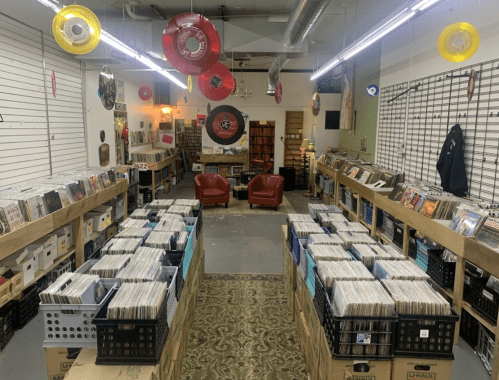 A cozy record store with rows of vinyl records, two red chairs, and colorful hanging decorations.