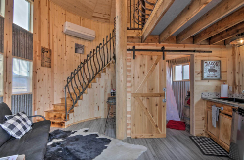 Cozy wooden interior of a cabin featuring a spiral staircase, a sofa, and a kitchen area with rustic decor.