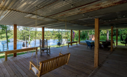 A rustic porch with a swing, overlooking a serene lake surrounded by trees.