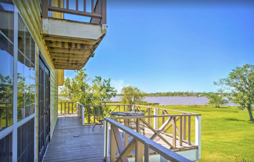 View from a balcony overlooking a serene lake, surrounded by greenery and a clear blue sky.