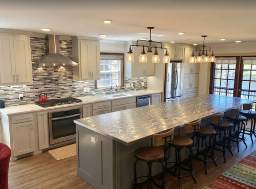 Modern kitchen with gray cabinets, a large island, pendant lights, and stainless steel appliances. Bright and spacious design.