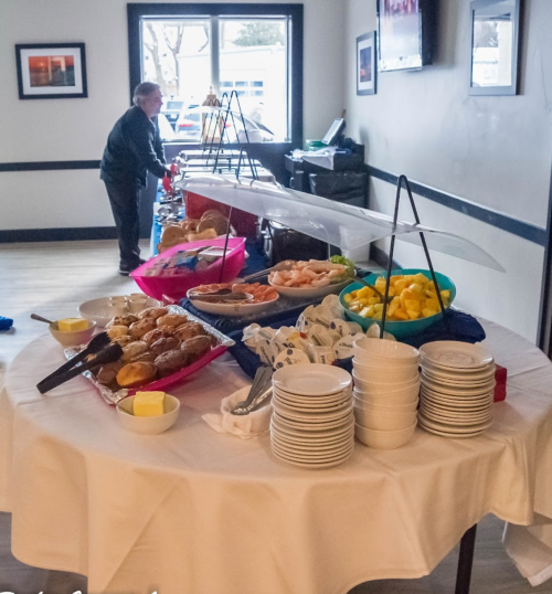 A buffet table with various food items, including pastries, fruit, and plates, with a person in the background.
