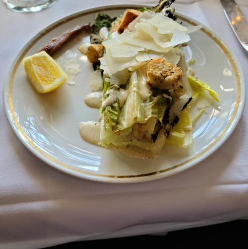 A plate with a Caesar salad featuring romaine lettuce, croutons, Parmesan cheese, and a lemon wedge.