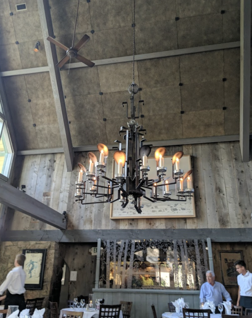 A rustic restaurant interior featuring a large chandelier and wooden beams, with diners and staff in the background.