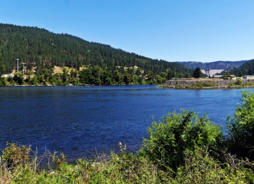 A serene river scene with lush green hills and a clear blue sky, reflecting the natural beauty of the landscape.