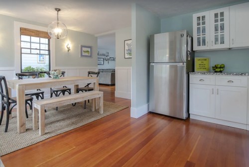 Bright kitchen and dining area with a wooden table, chairs, and stainless steel fridge, featuring light blue walls.