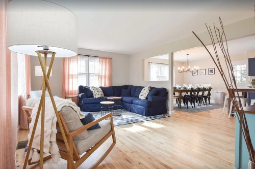 Bright living room with a blue sofa, wooden accents, and a dining area in the background, featuring a large table and chairs.