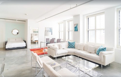 Bright, modern living space with a sectional sofa, glass coffee table, dining area, and large windows.