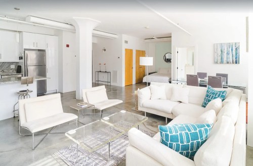 Bright, modern living space with a white sofa, glass tables, and a dining area, featuring minimalist decor and natural light.