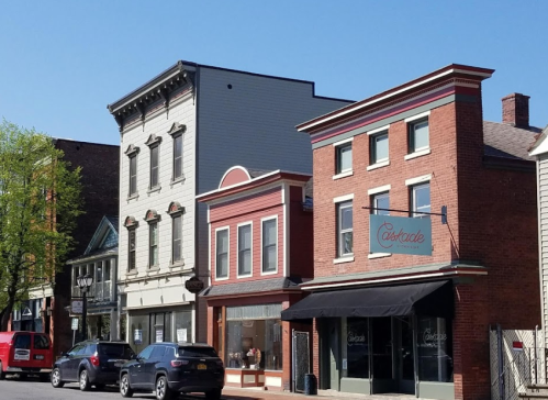 A row of historic buildings with shops, featuring brick and wooden facades, under a clear blue sky.