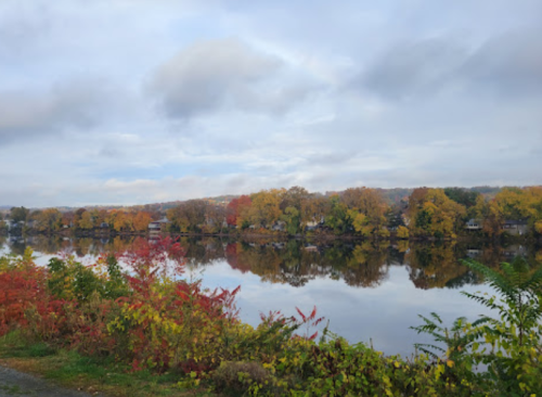 A serene river scene with colorful autumn foliage reflecting on the water under a cloudy sky.