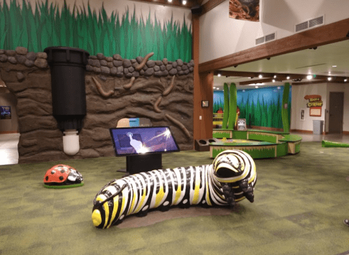 A colorful caterpillar sculpture in a children's play area with grass-themed walls and interactive displays.