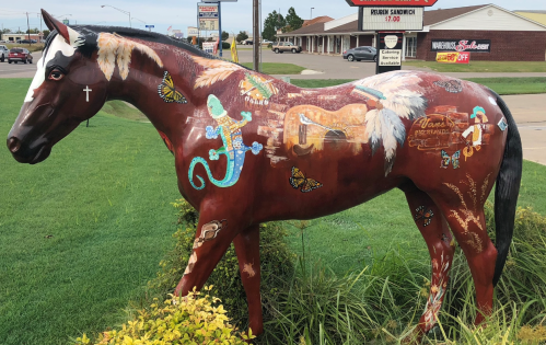 A painted horse statue adorned with colorful designs, including butterflies and lizards, set in a grassy area.