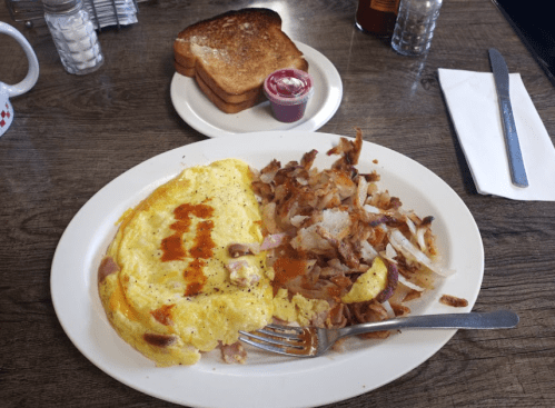 A plate with an omelette, hash browns, and a side of toast with jelly on a wooden table.
