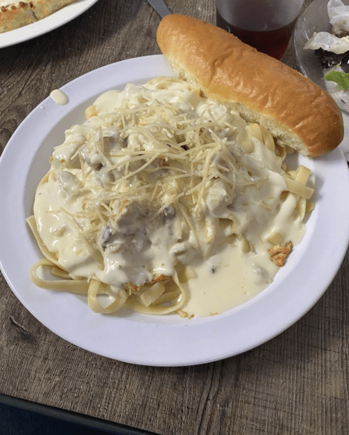 A plate of fettuccine pasta topped with creamy sauce and cheese, accompanied by a bread roll.