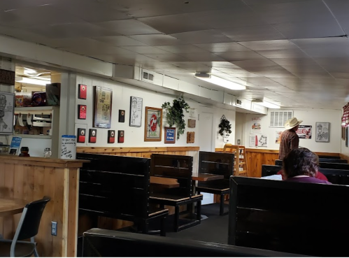Interior of a rustic diner with wooden booths, vintage decor, and a person in a hat standing in the background.