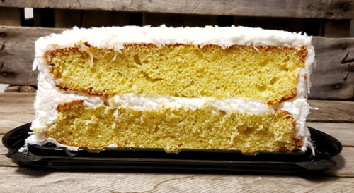 A sliced yellow cake with white frosting, displayed on a black tray against a rustic wooden background.