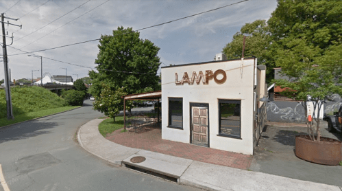 A small building with "LAMPO" signage, surrounded by greenery and a road, featuring outdoor seating.