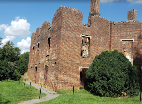 Ruins of a brick building with broken windows, surrounded by greenery and a clear blue sky.