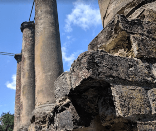 Close-up of weathered stone ruins with tall columns against a blue sky with scattered clouds.