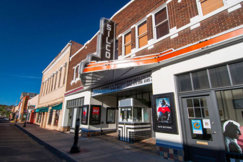 Historic Silco Theater building with a marquee, colorful storefronts, and clear blue sky in the background.