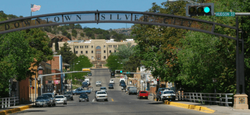 View of a street in downtown Silver City, New Mexico, with trees, cars, and a sign arching over the road.