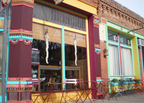 Colorful storefront with decorative windows and outdoor seating, featuring vibrant patterns and a welcoming atmosphere.